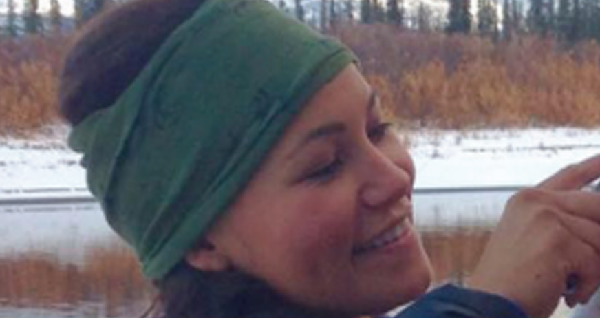 Smiling woman in green headband near a lake with autumn colors and snow in the background.
